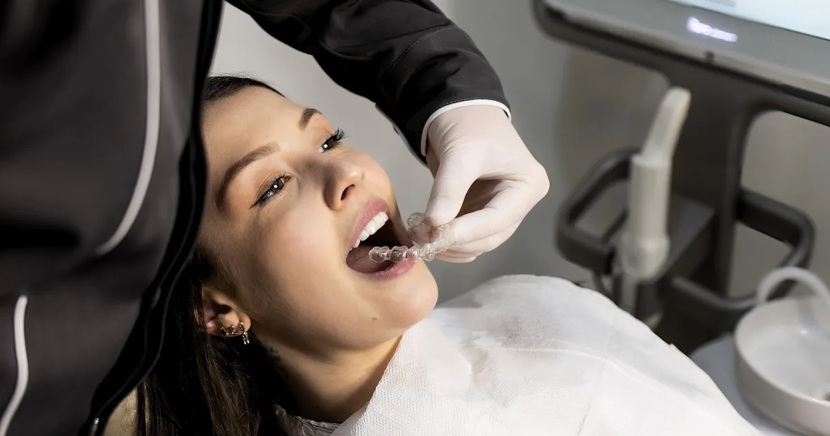 Dental patient having a clear aligner tray fitted while a 3D digital model of her teeth is displayed on the monitor behind her — digital smile design at Family Dentist of Palm Beach, Royal Palm Beach, FL